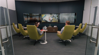 People collaborating in a room with multiple TV screens and big green chairs 