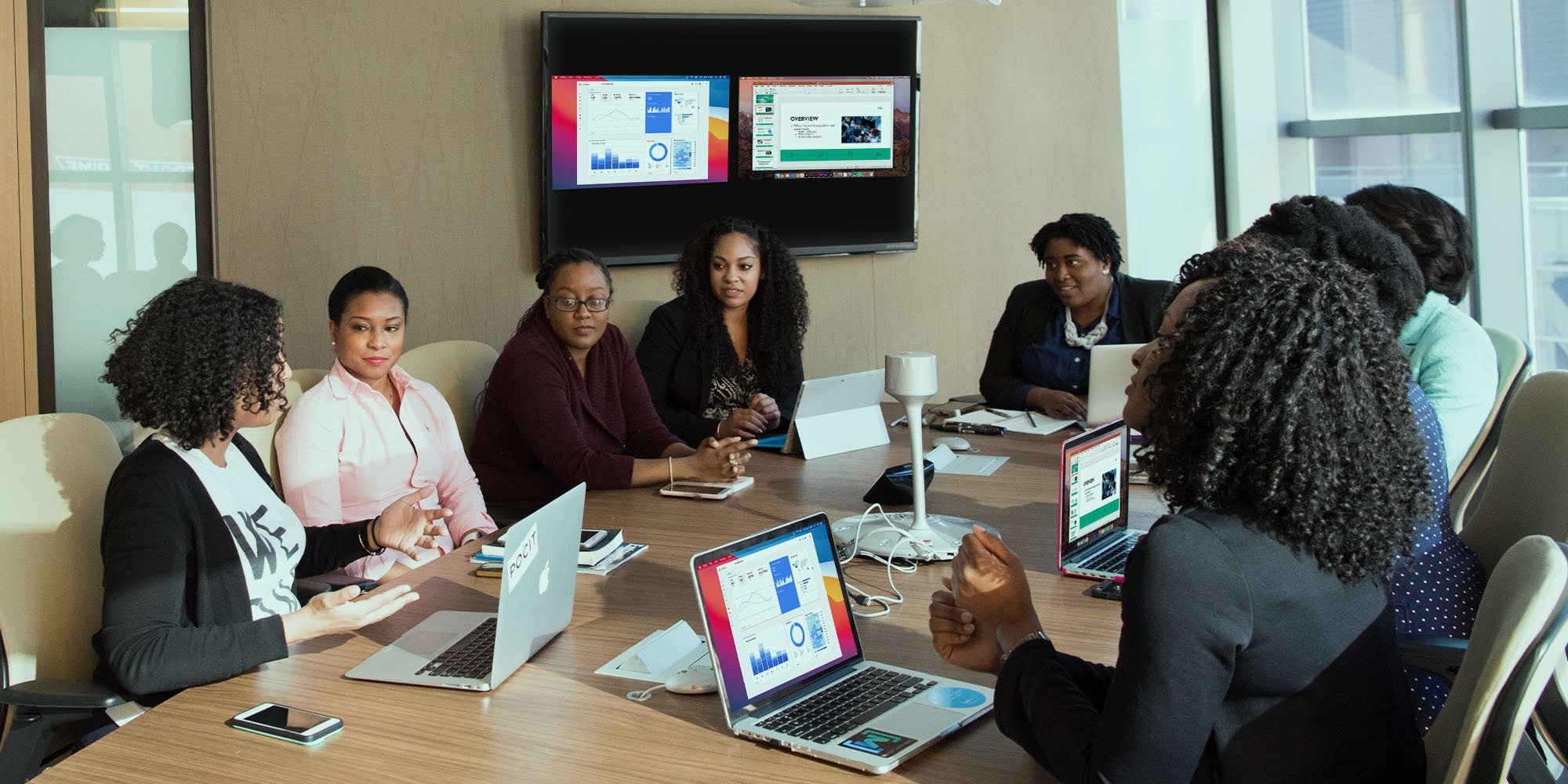 People meeting in a conference room while sharing wirelessly from two computers to a large TV screen