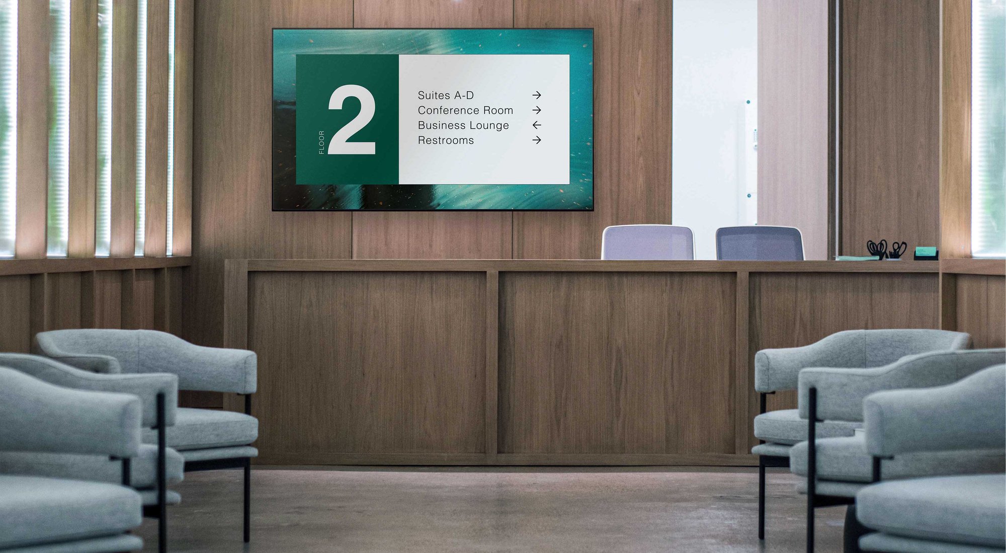 A modern reception area with a digital sign displaying directions for floor 2, including suites, a conference room, business lounge, and restrooms.