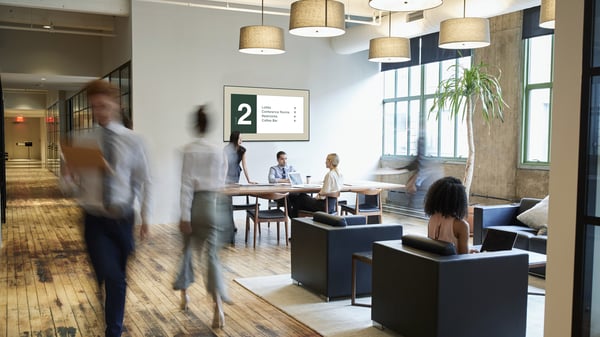 Digital signage on a screen in an office with people walking by